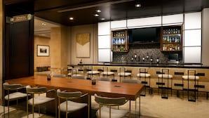 A conference room with a long wooden table and multiple chairs, a bar area with shelves of bottles, and a television mounted on the wall. - Sheraton Garden Grove-Anaheim South Hotel (Garden Grove)
