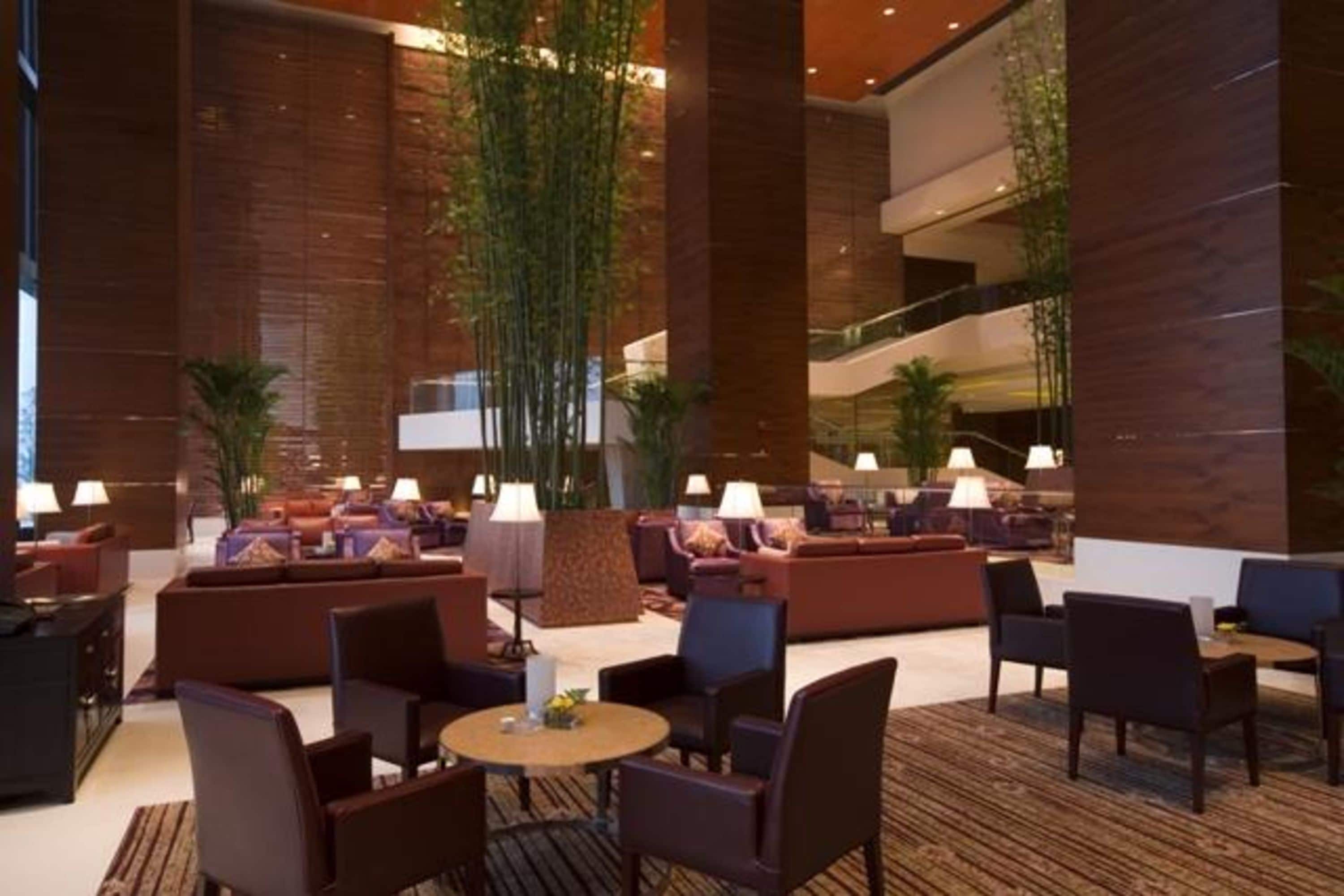 A spacious lobby with multiple seating areas, including sofas and chairs, and a central column with plants.