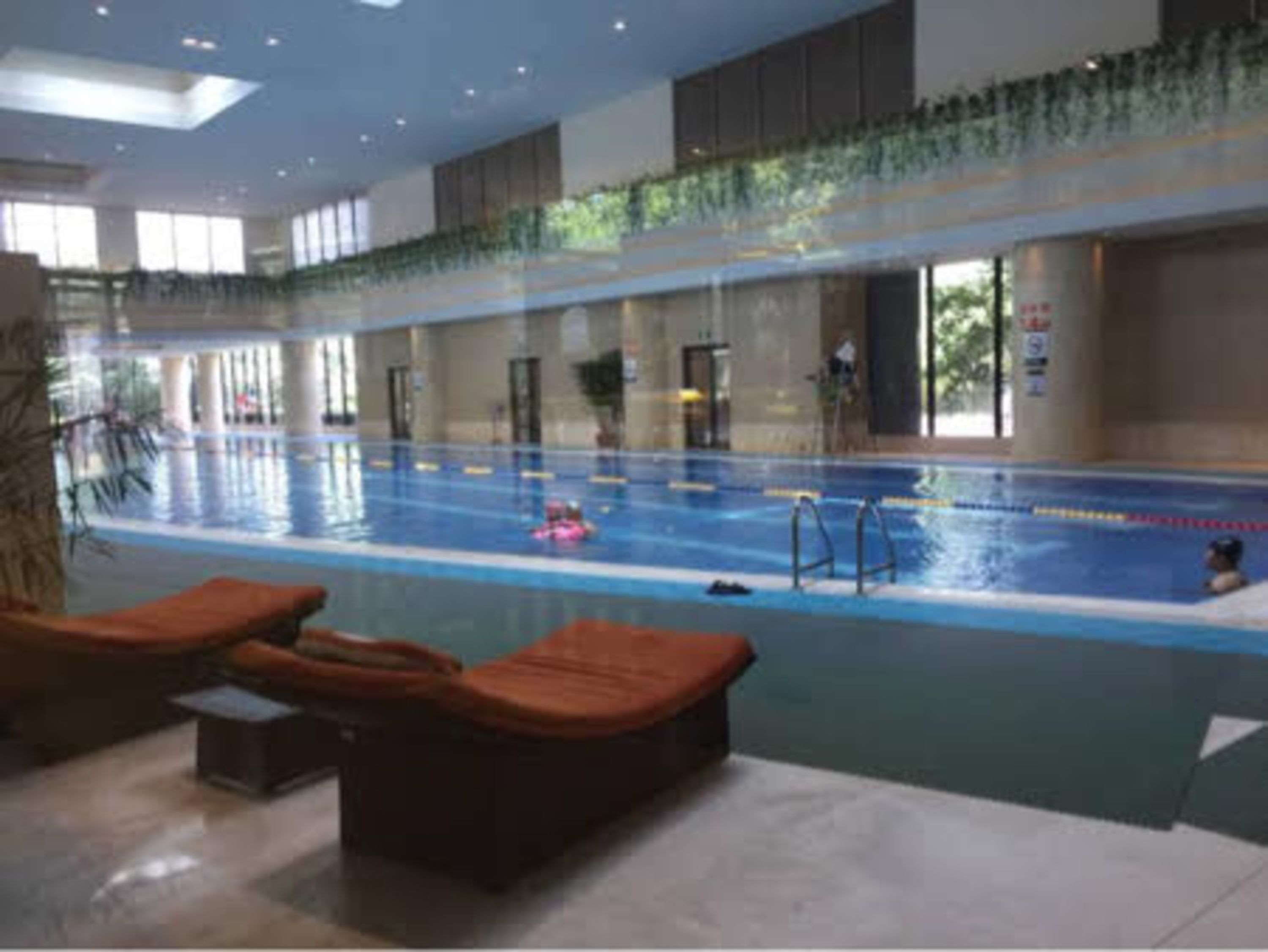 Una piscina interior con carriles delimitados, sillas de descanso e iluminación empotrada en el techo.