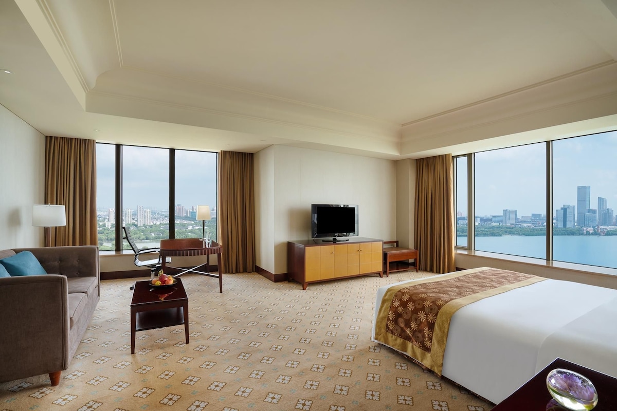Habitación de hotel con una cama grande, un sofá, un escritorio, un televisor y vistas a un paisaje urbano.