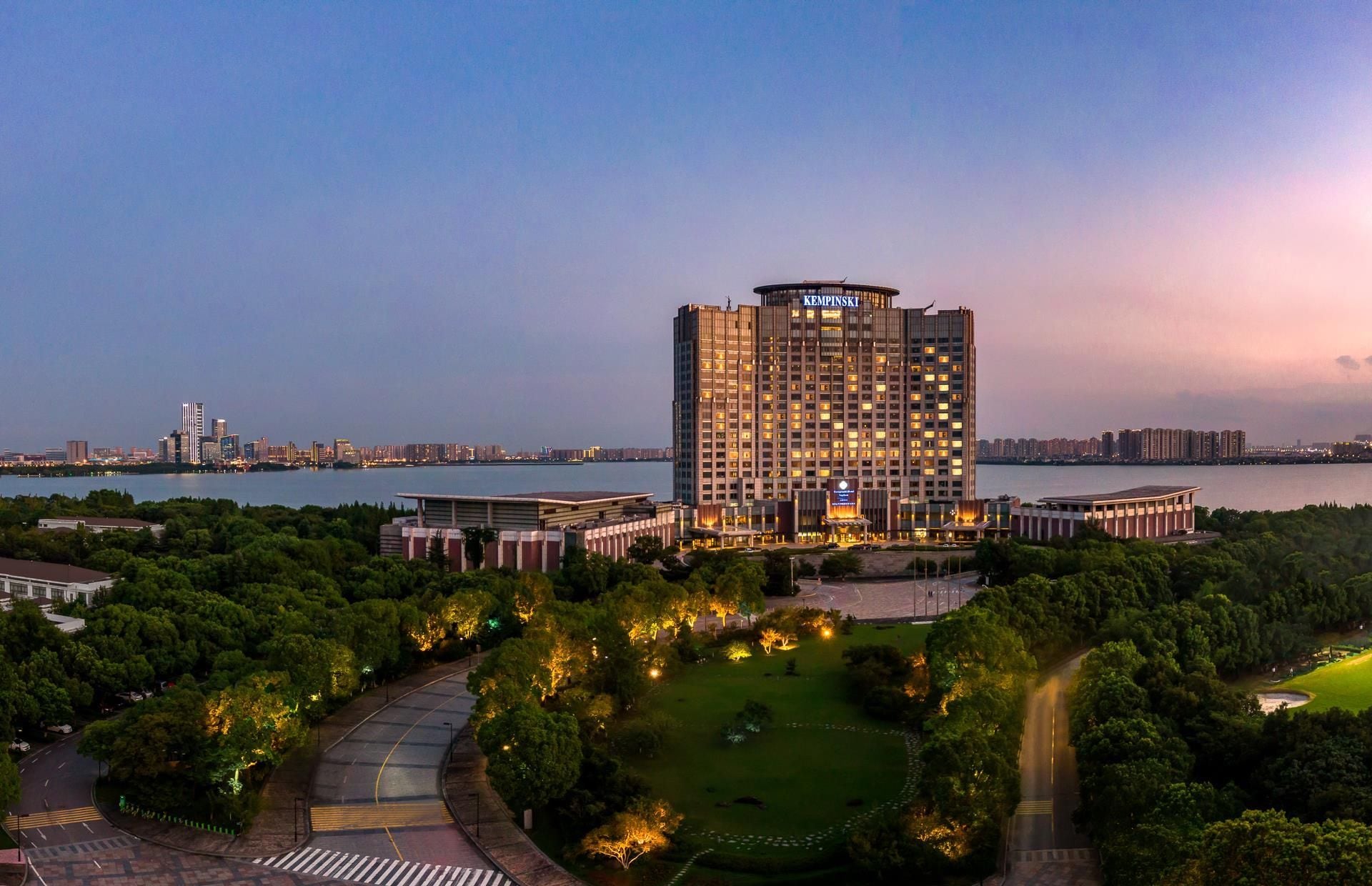 A high-rise hotel with a view of a river and city skyline at dusk.