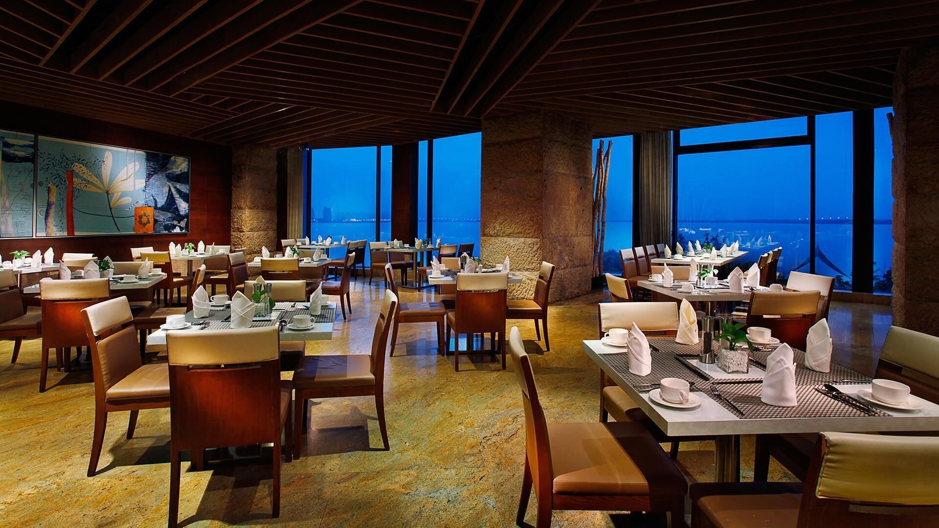 Un'ampia sala da pranzo con diversi tavoli e sedie, grandi finestre con vista sul mare e un affresco sulla parete.