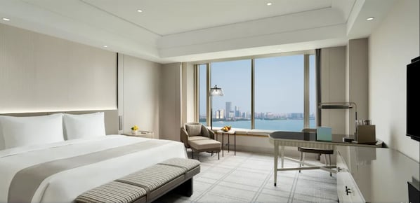Habitación de hotel moderna con una cama grande, un escritorio, una silla y vistas a la silueta urbana.