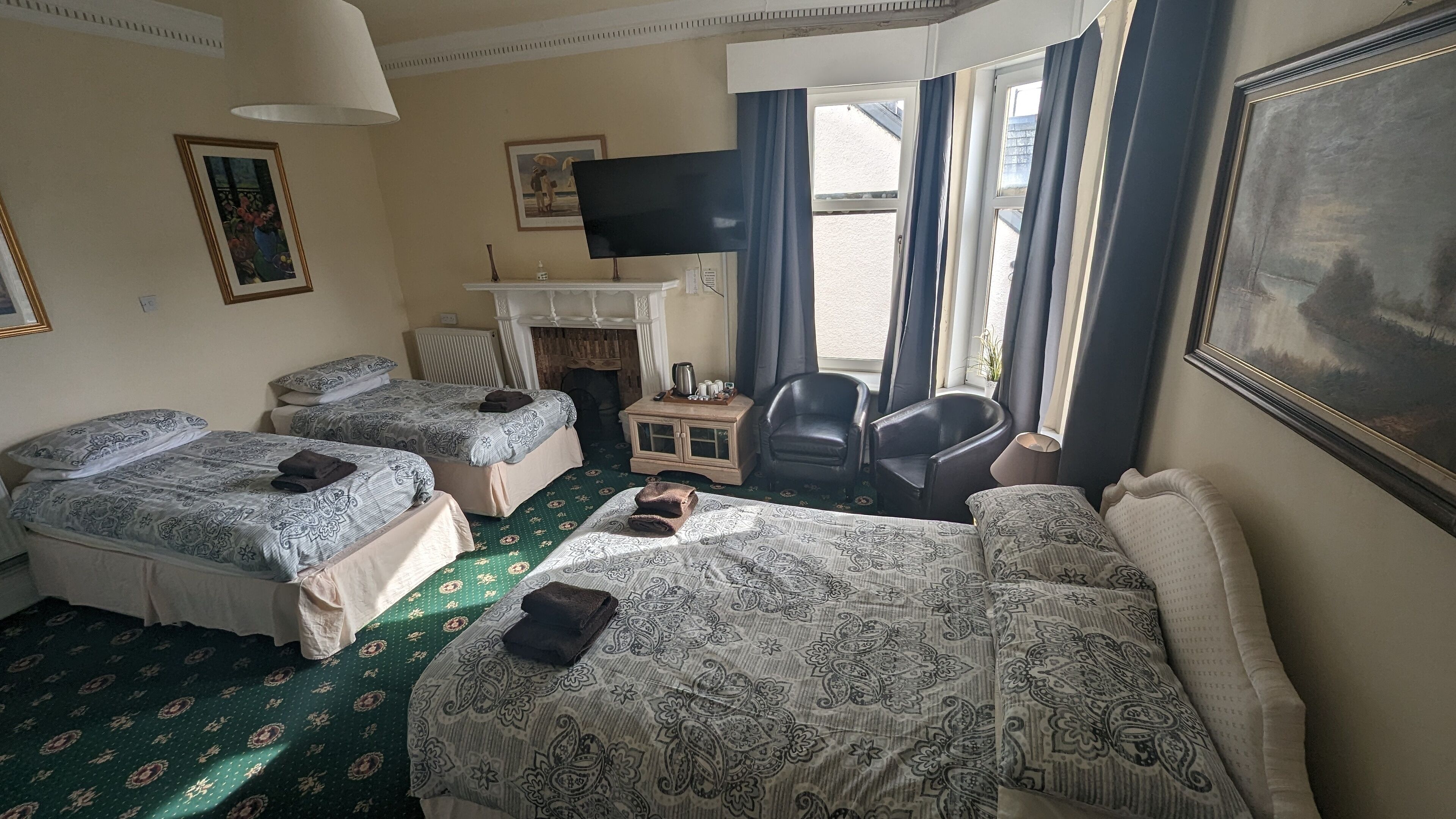 Habitación de hotel con dos camas individuales, un sofá, un televisor, una mesita de noche con lámpara y una silla.