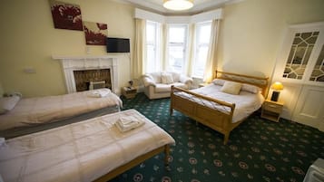 Een hotelkamer met twee enkele bedden, een zithoek met een fauteuil, een open haard en een groot raam met gordijnen.