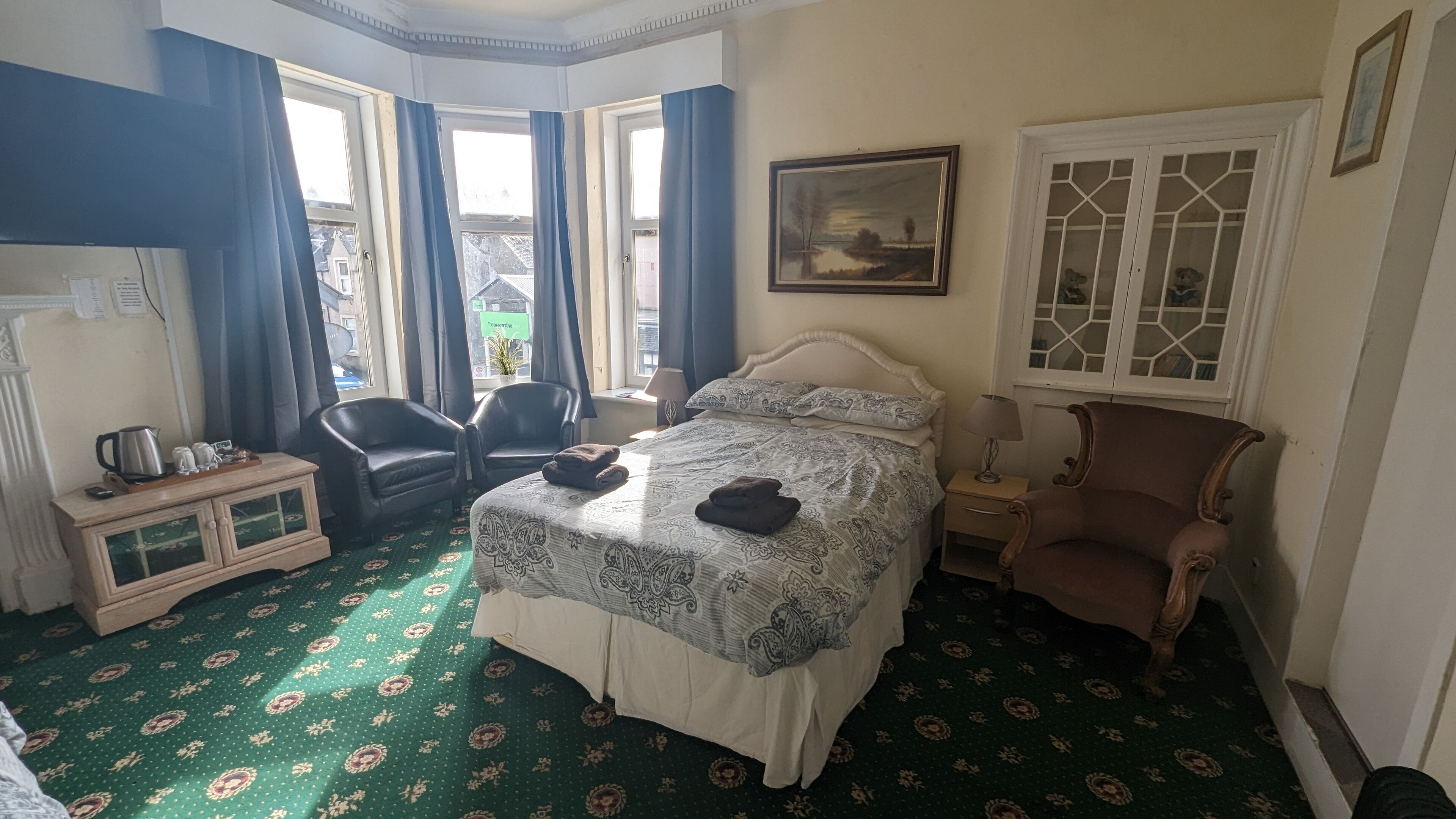 Una camera d'albergo con un letto, due poltrone, un piccolo armadietto e una finestra con tende.