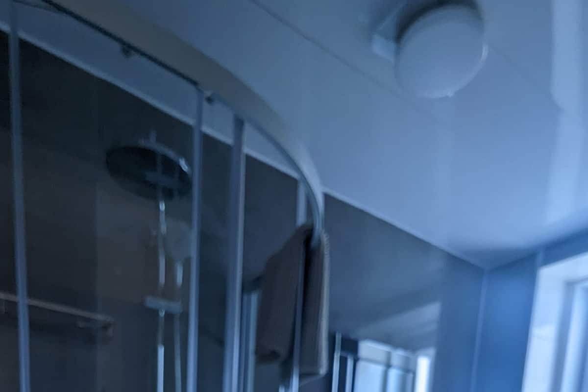 Kylpyhuone, jossa on lasiseinäinen suihkukaappi, pesuallas ja peili.