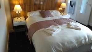 Une chambre d’hôtel avec un grand lit, deux lampes de chevet, une tête de lit en bois et une fenêtre avec des stores.