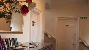 Un espace d’accueil avec un bureau en verre, des livres, un miroir et un escalier menant à un ascenseur.