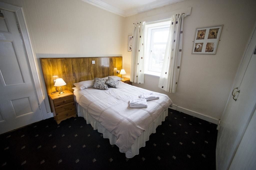 A neatly made bed with a wooden headboard, two bedside lamps, and a window with curtains.