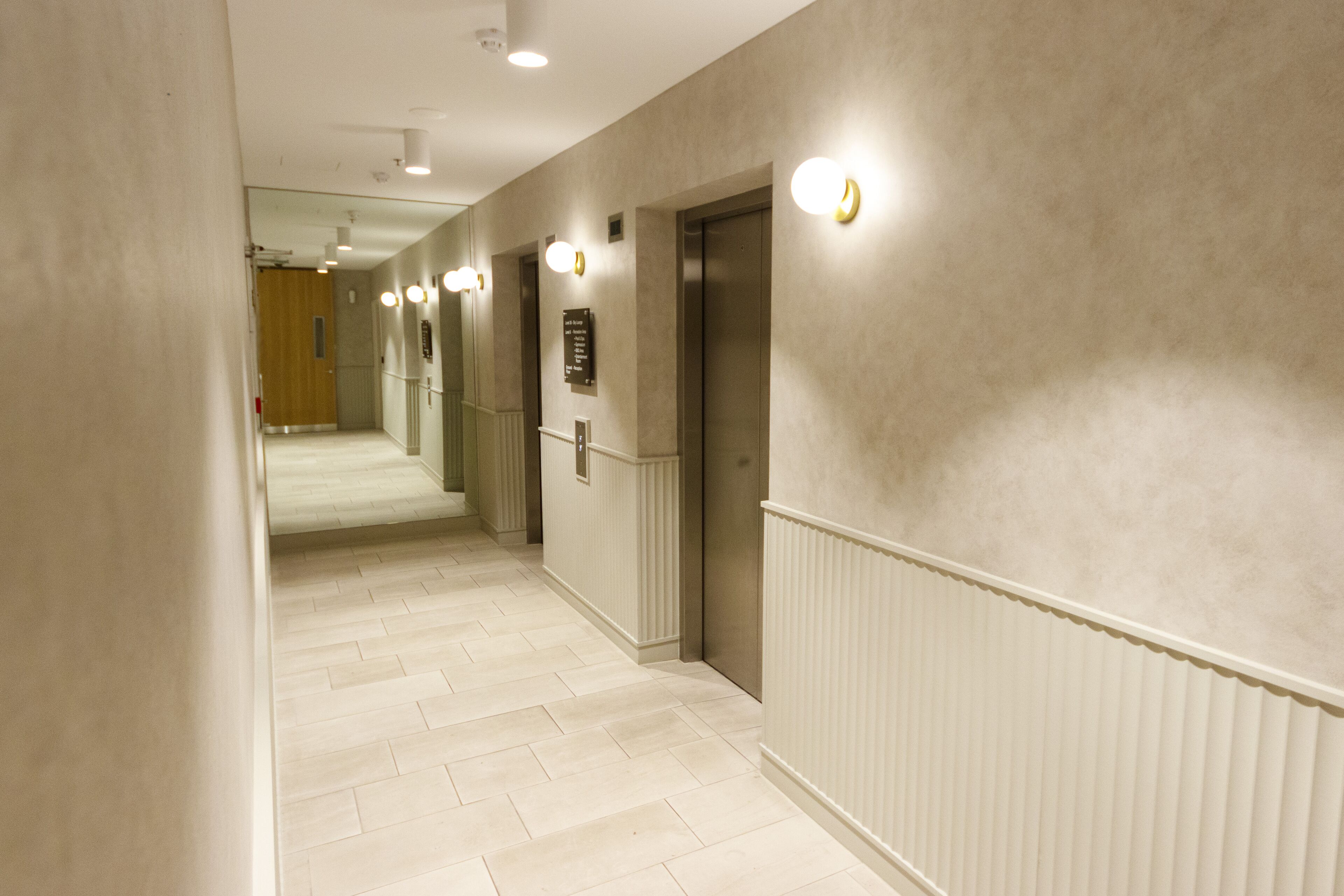 A hallway with a light-colored floor, white walls, and a radiator. There are two doors, one of which is an elevator.