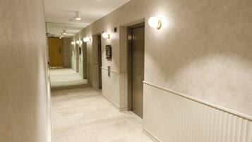 A hallway with a light-colored floor, white walls, and a radiator. There are two doors, one of which is an elevator.