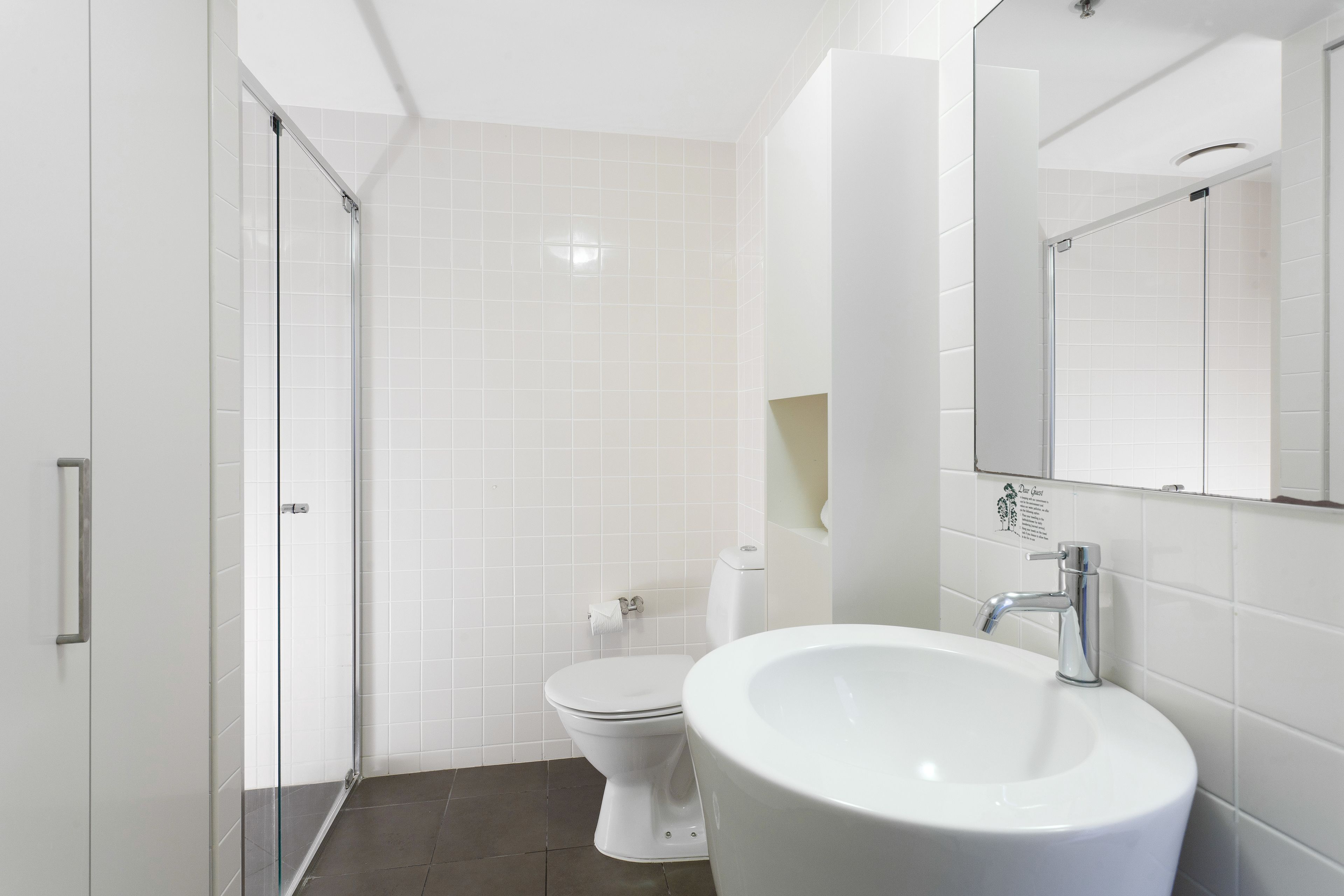 Un bany modern amb un espai de dutxa amb mampara de vidre, un vàter blanc i un lavabo amb mirall.
