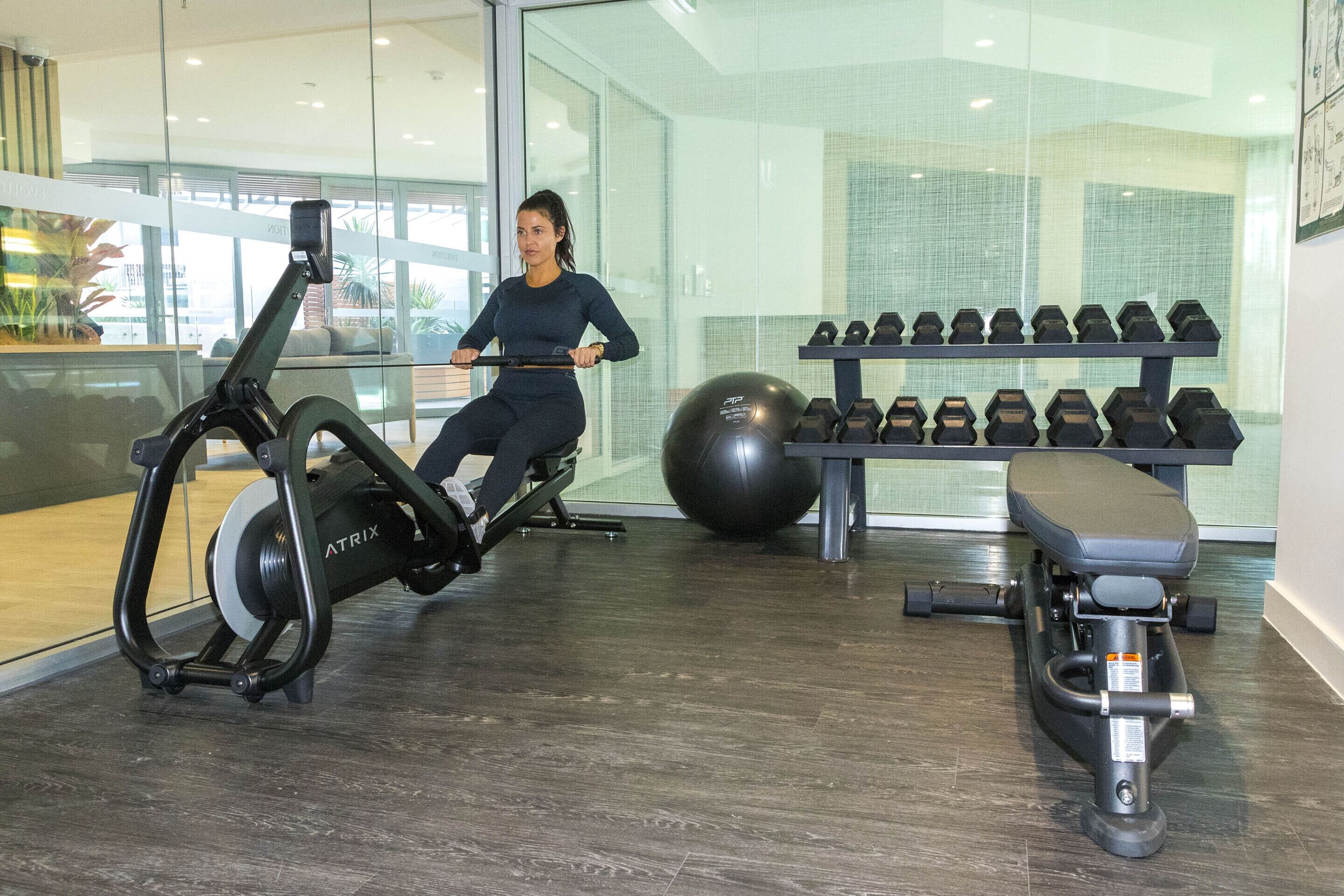 Een sportschool met cardioapparatuur, gewichten en een hometrainer.