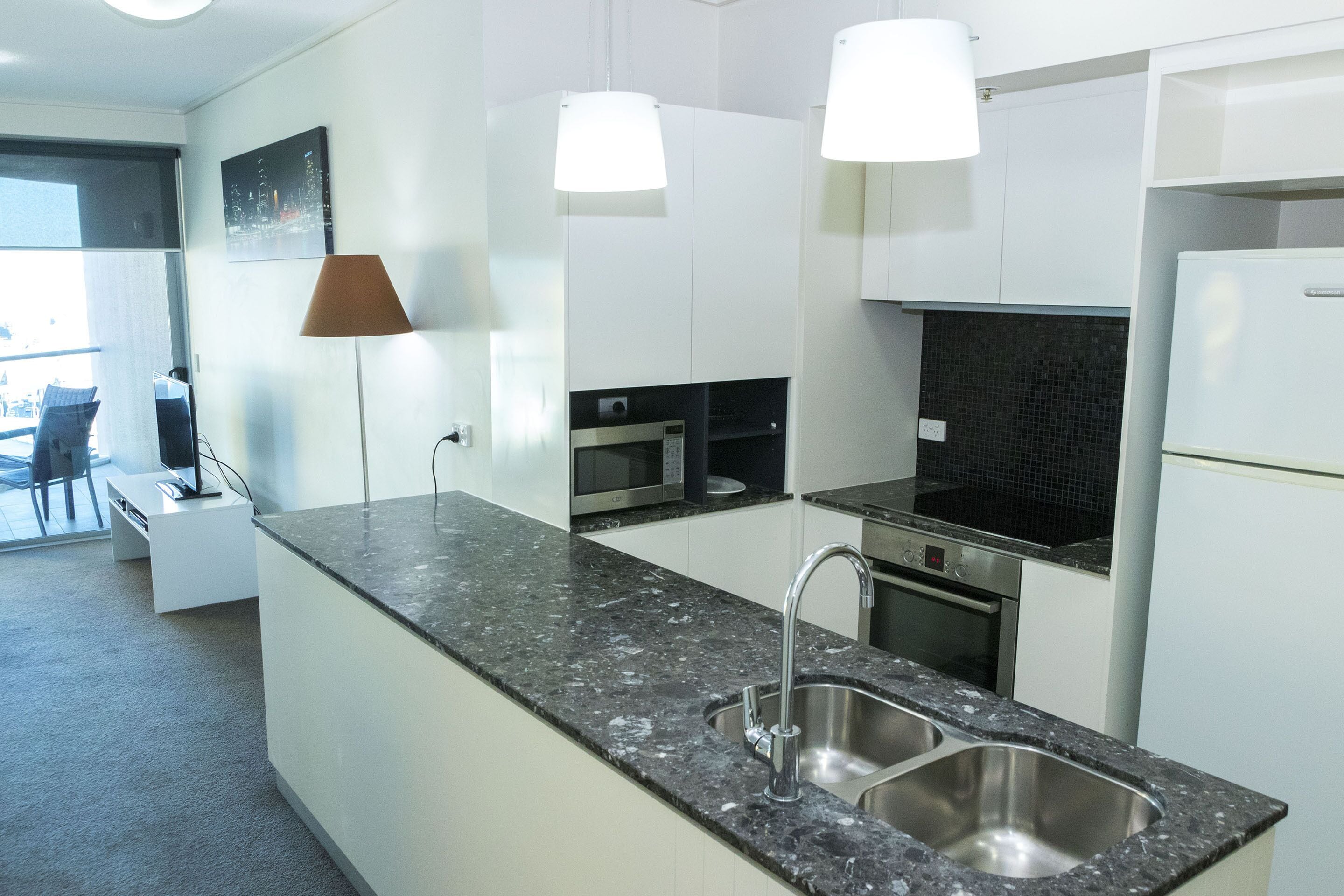 Una cocina moderna con encimera de granito, pileta de acero inoxidable y muebles altos blancos. Se ve un comedor al fondo con una mesa y sillas.