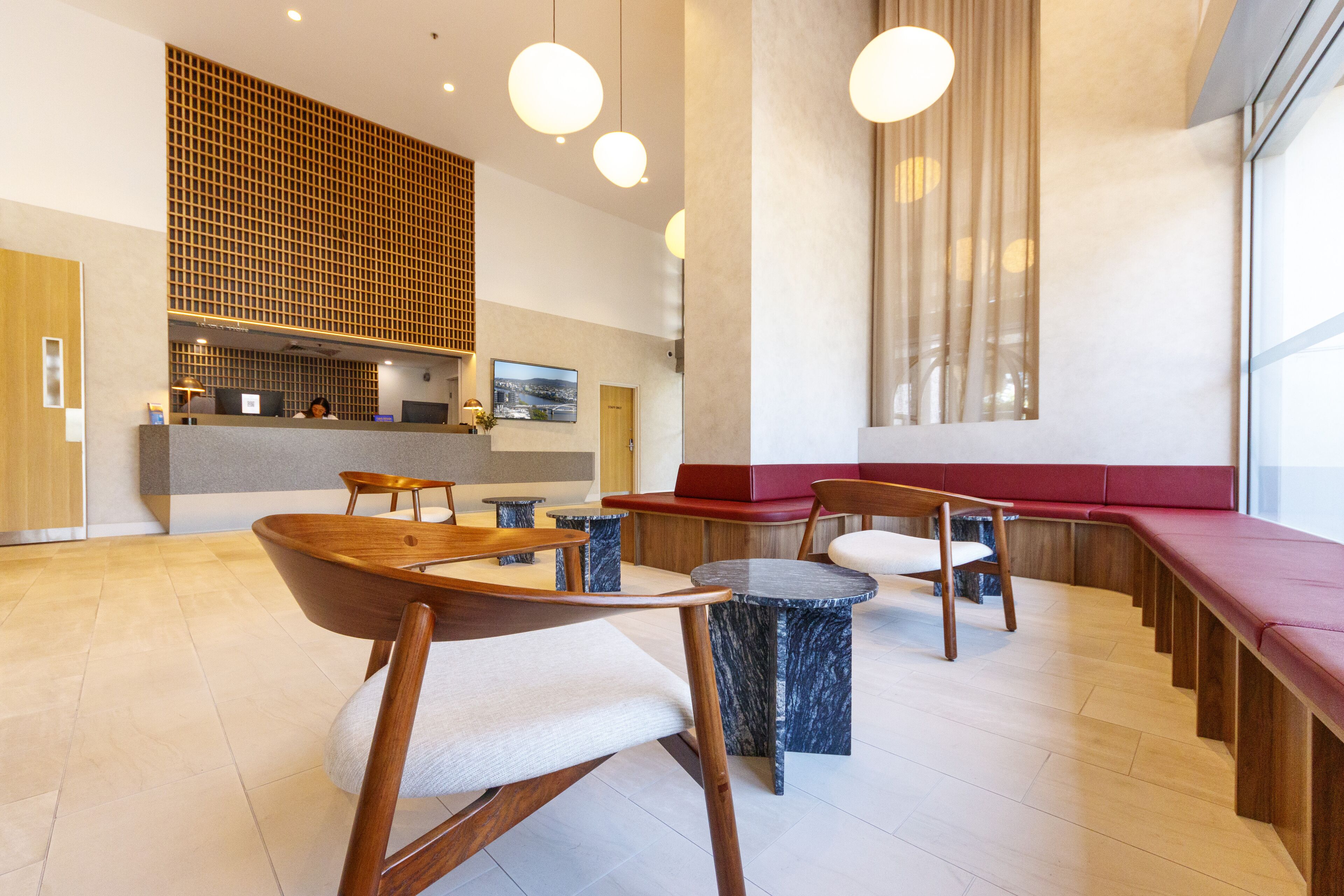 A modern interior with wooden furniture, marble tables, and a seating area with red cushions.