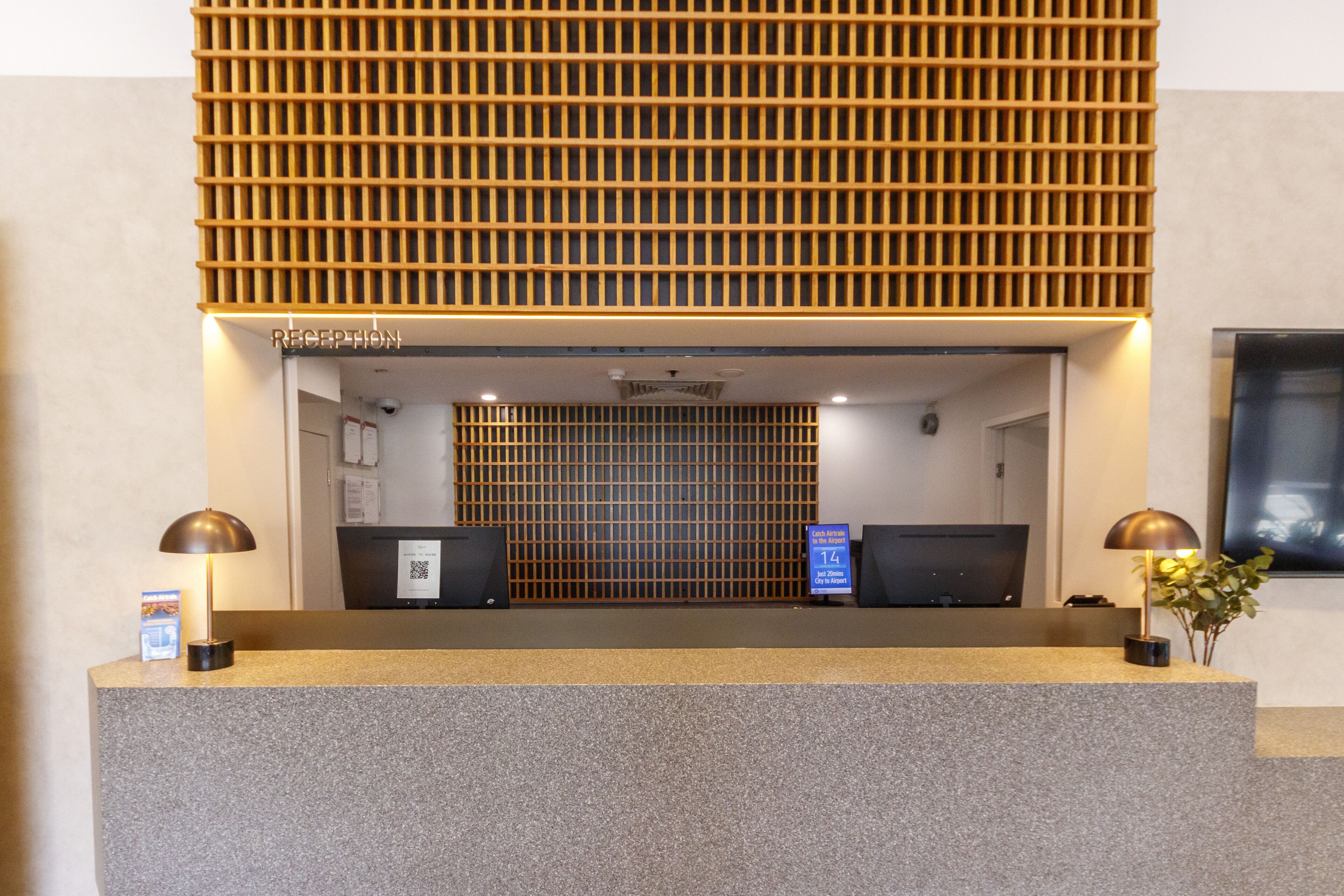 A reception desk with a modern design, featuring a wooden slatted partition above and two black monitors on either side.