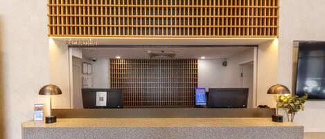 A reception desk with a modern design, featuring a wooden slatted partition above and two black monitors on either side.