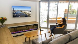 A modern living room with a fireplace, a large flat-screen TV, and a view of the outdoors through large glass doors. - Evolution Apartments (Brisbane)