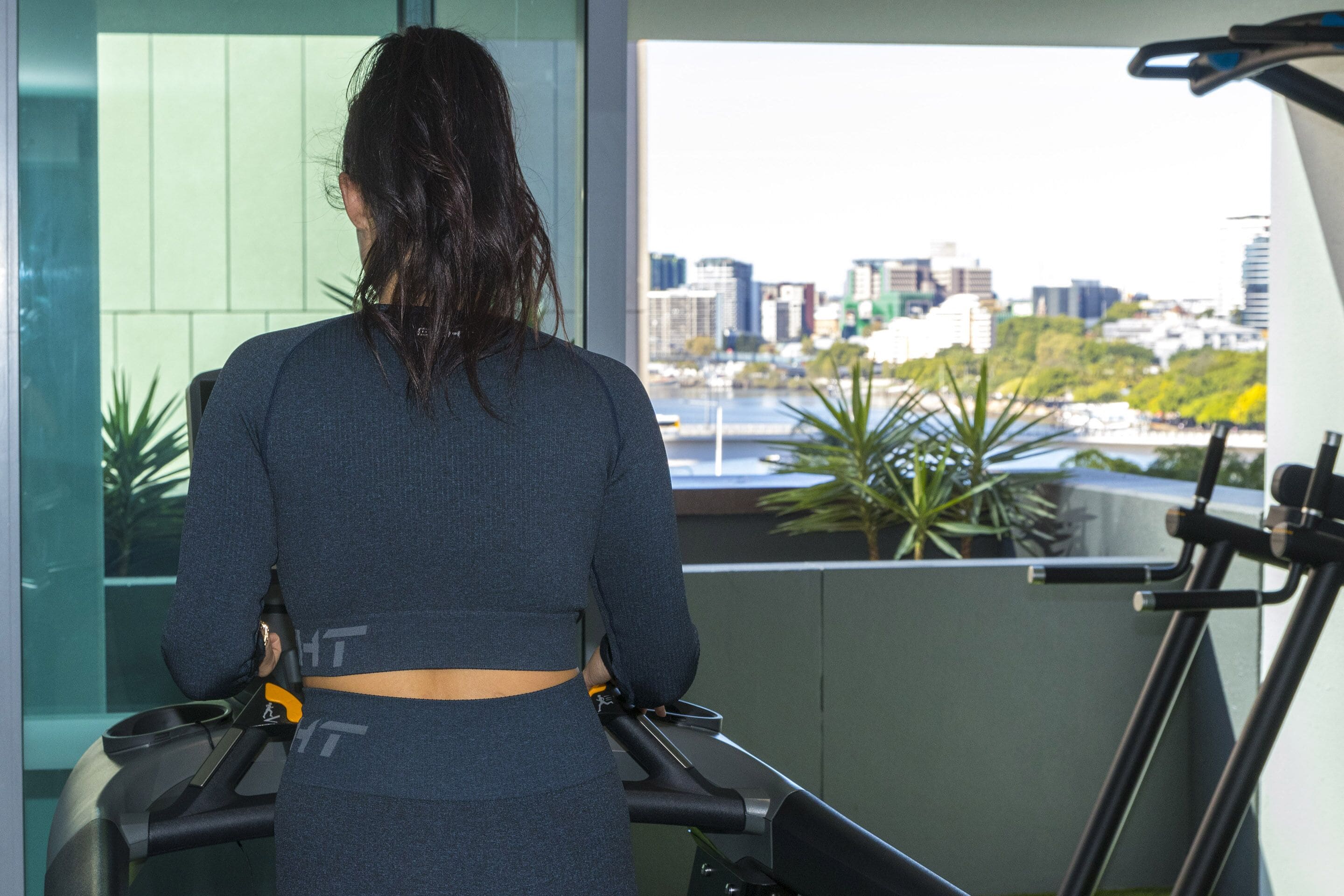 A person using a treadmill in a room with a large window overlooking a cityscape.
