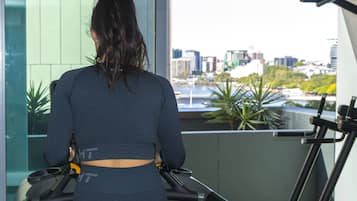 A person using a treadmill in a room with a large window overlooking a cityscape.