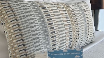 Una cama bien hecha con un edredón y almohadas estampadas, un certificado de limpieza y un atomizador para dormir.