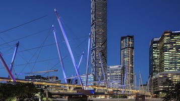 Un paisaje urbano moderno con un rascacielos cilíndrico destacado, un puente con cables morados y edificios de gran altura aledaños.