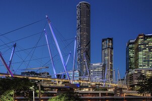 A modern cityscape with a prominent cylindrical skyscraper, a bridge with purple cables, and adjacent high-rise buildings.