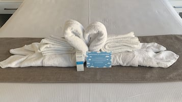 A neatly made bed with a towel arrangement in the shape of a heart, a certificate of cleanliness, and a remote control on the nightstand.