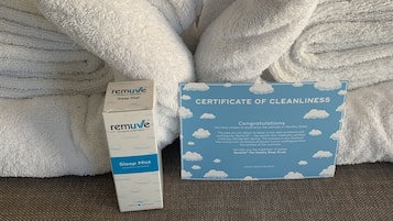 A neatly folded white towel and a certificate of cleanliness on a bed with a white headboard and pillows.