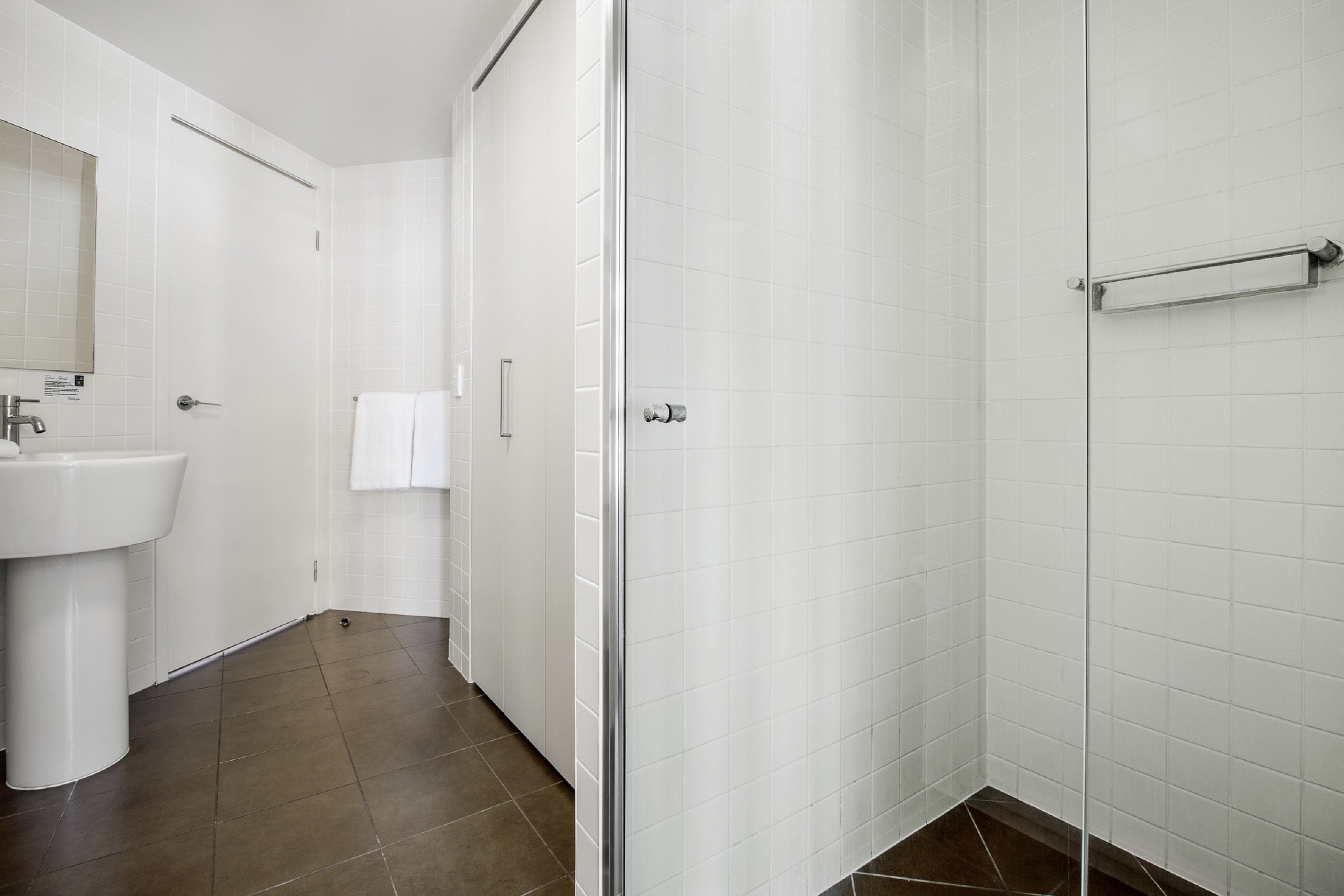 A modern bathroom with a white sink, a glass shower enclosure, and a tiled floor.