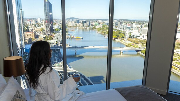 A hotel room with a large window offering a view of a cityscape, including a river and bridges. - Evolution Apartments (Brisbane)