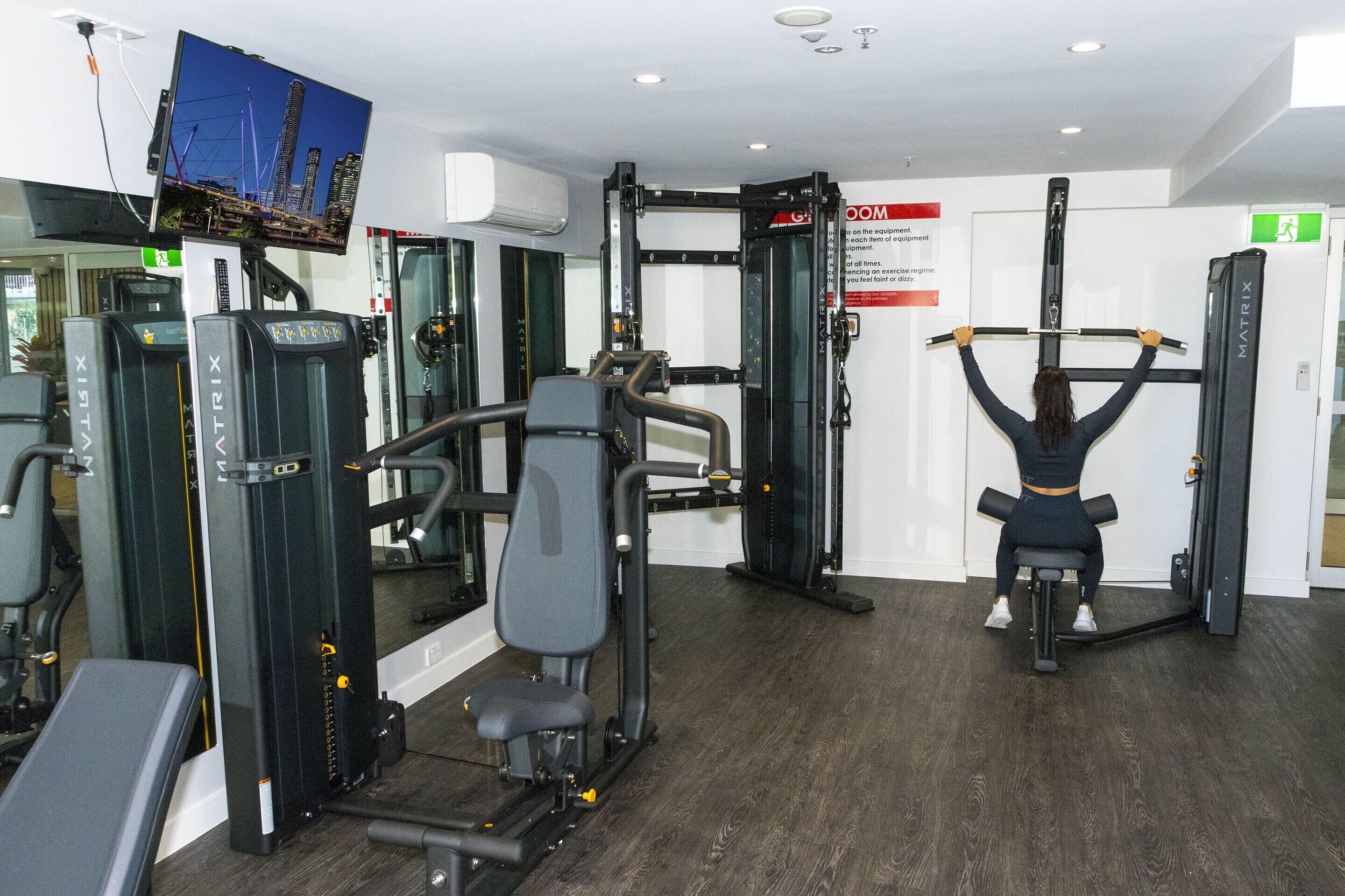 A gym with various exercise machines, a pull-up bar, and a television mounted on the wall.