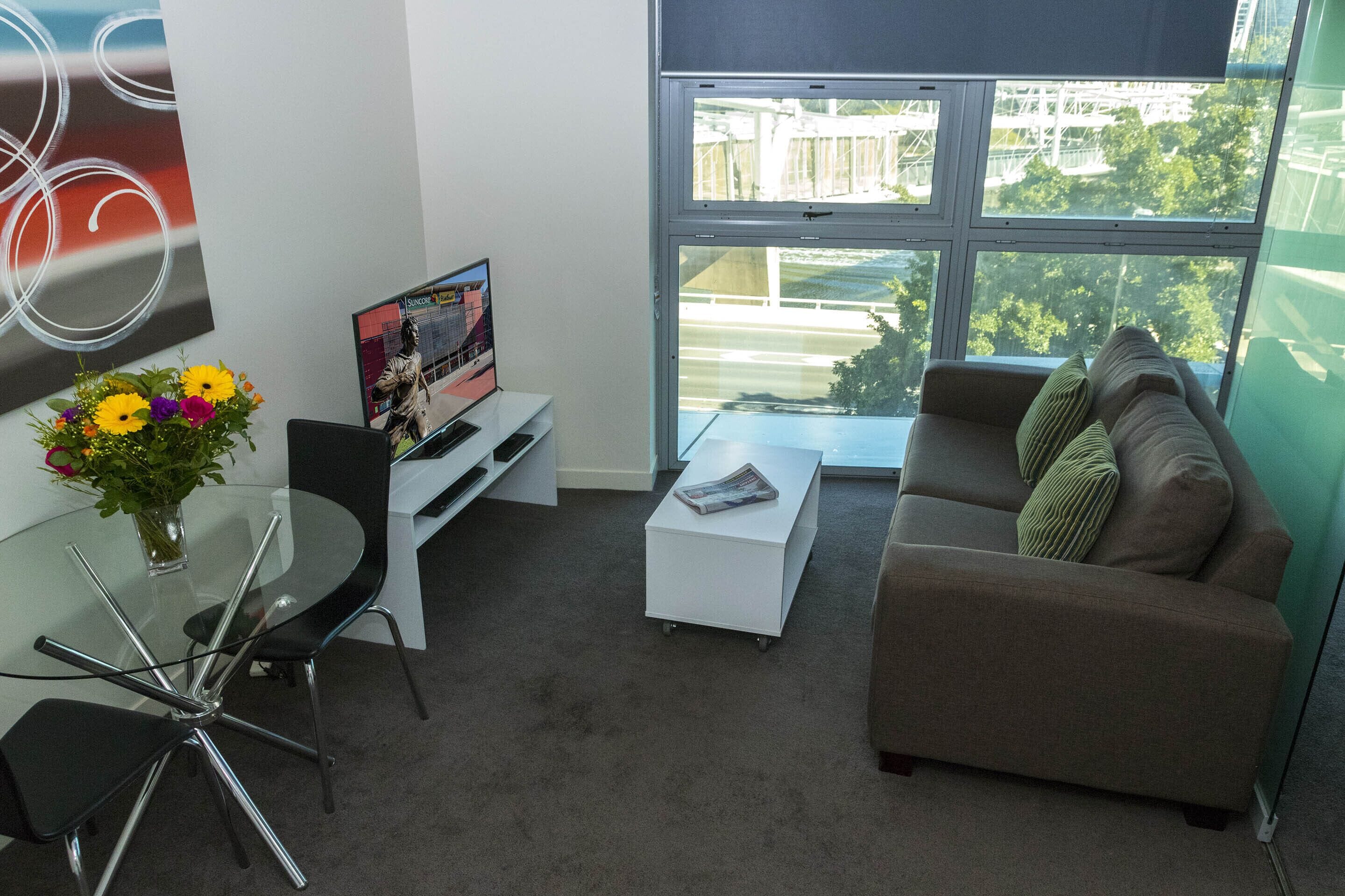 A modern living room with a glass table, a sofa, a coffee table, and a TV on a stand.