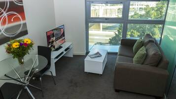 A modern living room with a glass table, a sofa, a coffee table, and a TV on a stand.