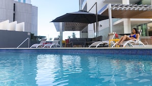 A pool area with lounge chairs and an umbrella. - Evolution Apartments (Brisbane)