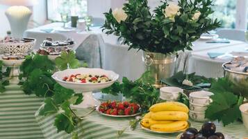 A table set with various fruits and a vase of flowers, with a striped tablecloth and a marble floor.