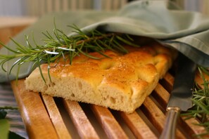 A slice of bread on a wooden cutting board with a knife and rosemary sprigs. - Hotel Eveline Portosole (Sanremo)