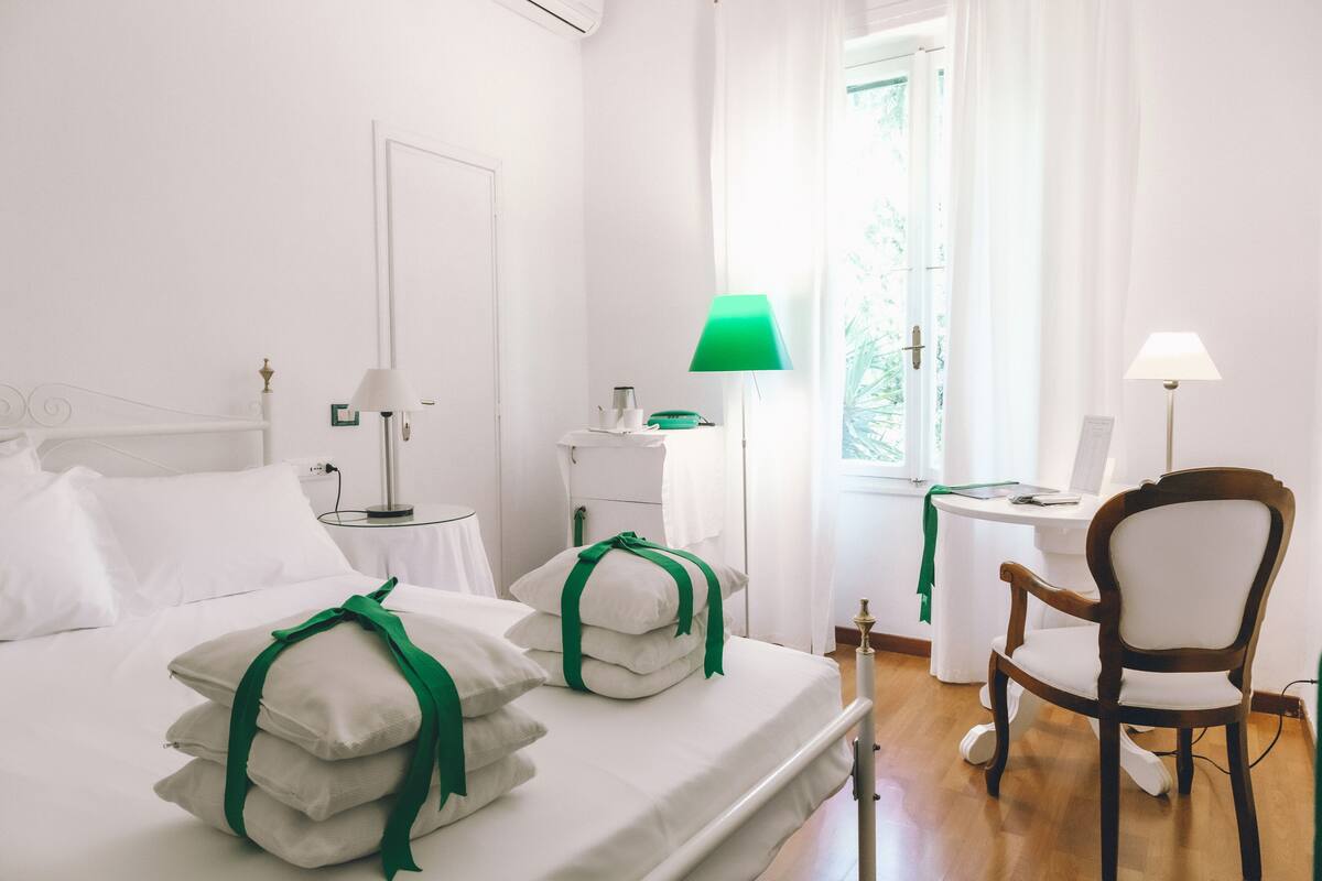 Una habitación de hotel con una cama bien hecha, una silla de madera, un escritorio con lámpara y una ventana con cortinas.
