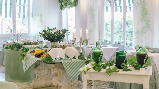 Un espace repas avec des tables dressées pour le repas, agrémenté de nappes vertes et blanches, de bougies et de plantes.