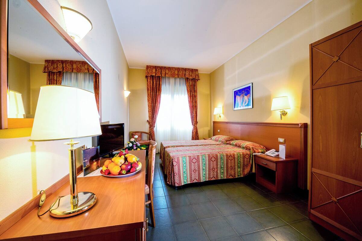 Une chambre d’hôtel avec un lit, une table de chevet, une lampe et un panier de fruits.