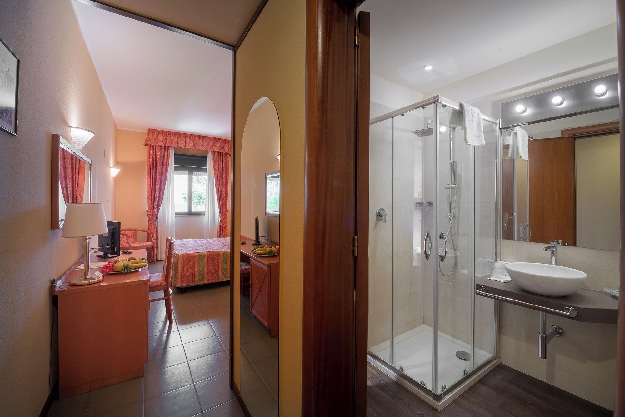 A hotel room with a bed, desk, and a shower area with a glass door.
