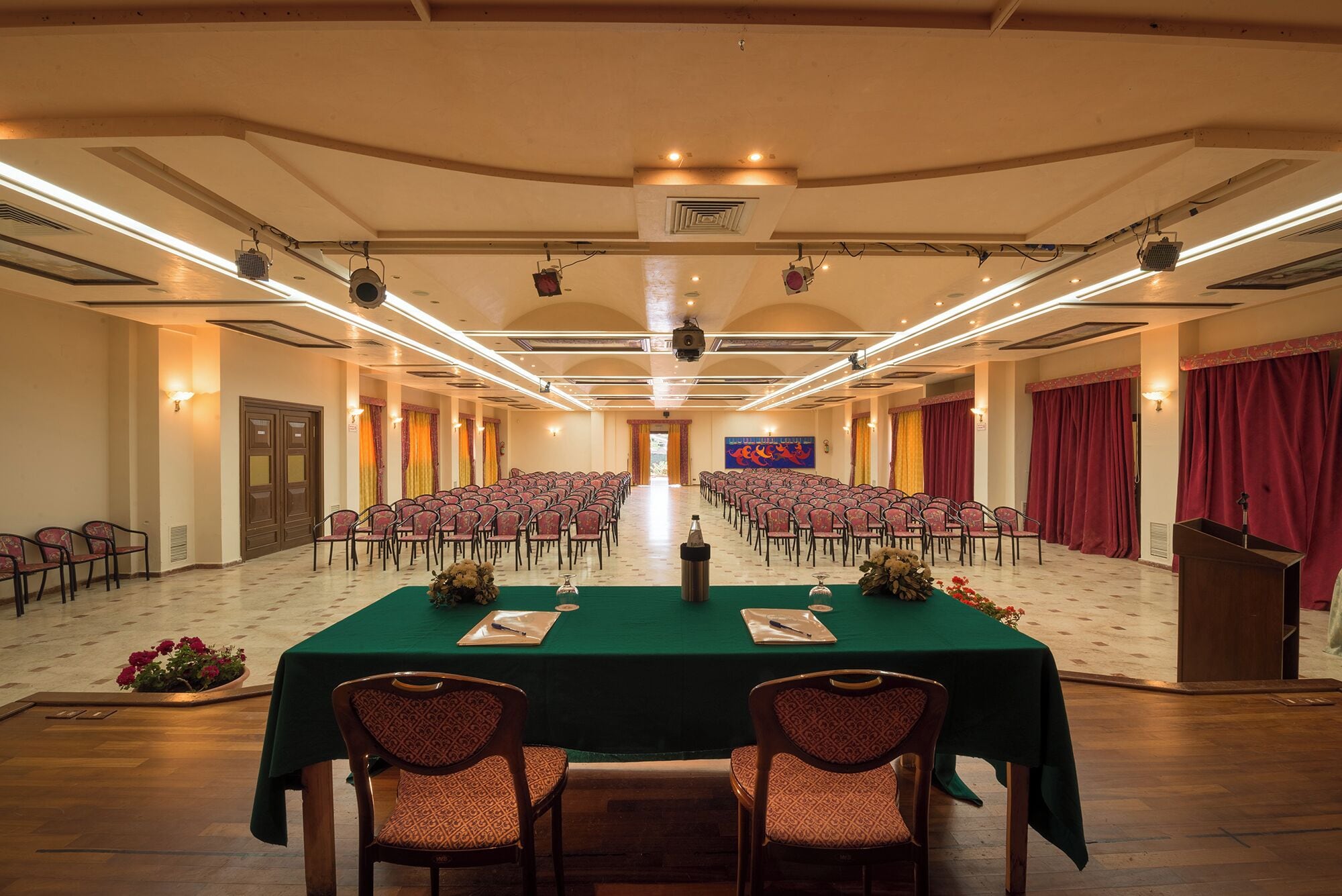 Un salón de conferencias con filas de sillas, un atril y un escenario con una bandera.