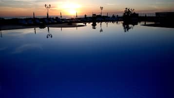 Un'area piscina tranquilla con lettini e lampioni, che riflettono il tramonto.