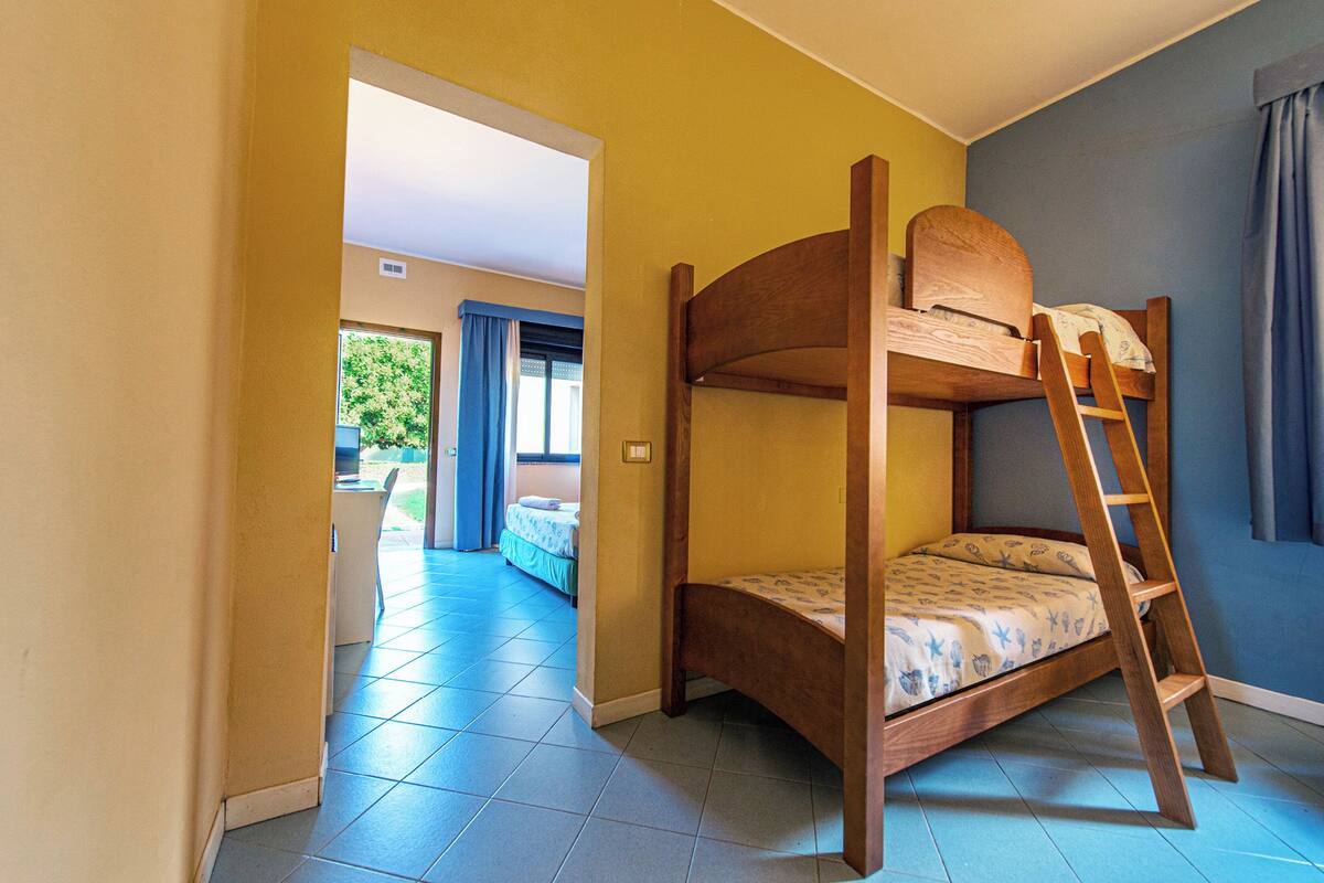 Un lit superposé avec une échelle en bois, un sol carrelé et une vue sur un espace extérieur avec une porte et des rideaux.
