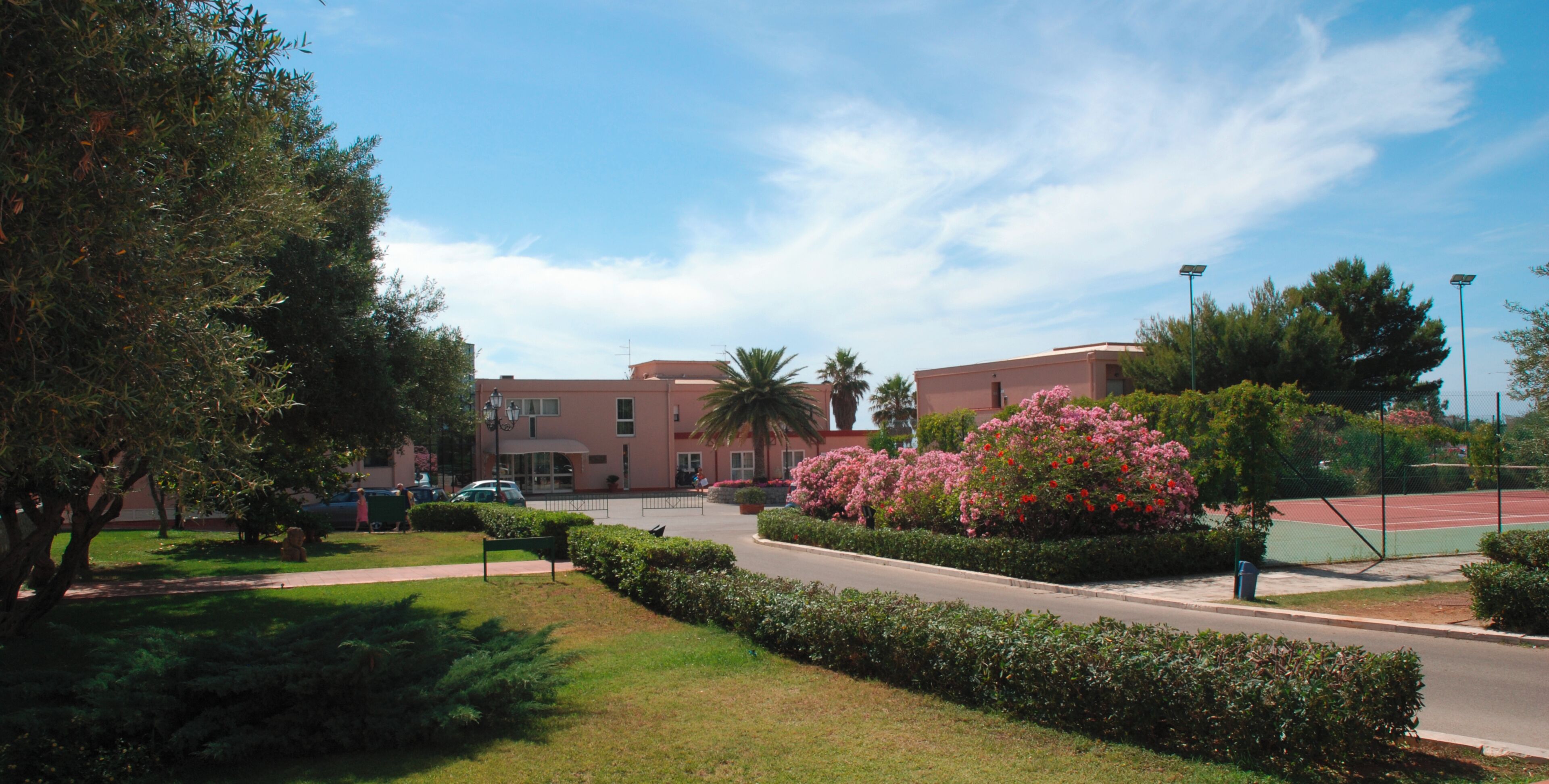 Un edificio con facciata rossa, un campo da tennis e un giardino curato con diverse piante e fiori.