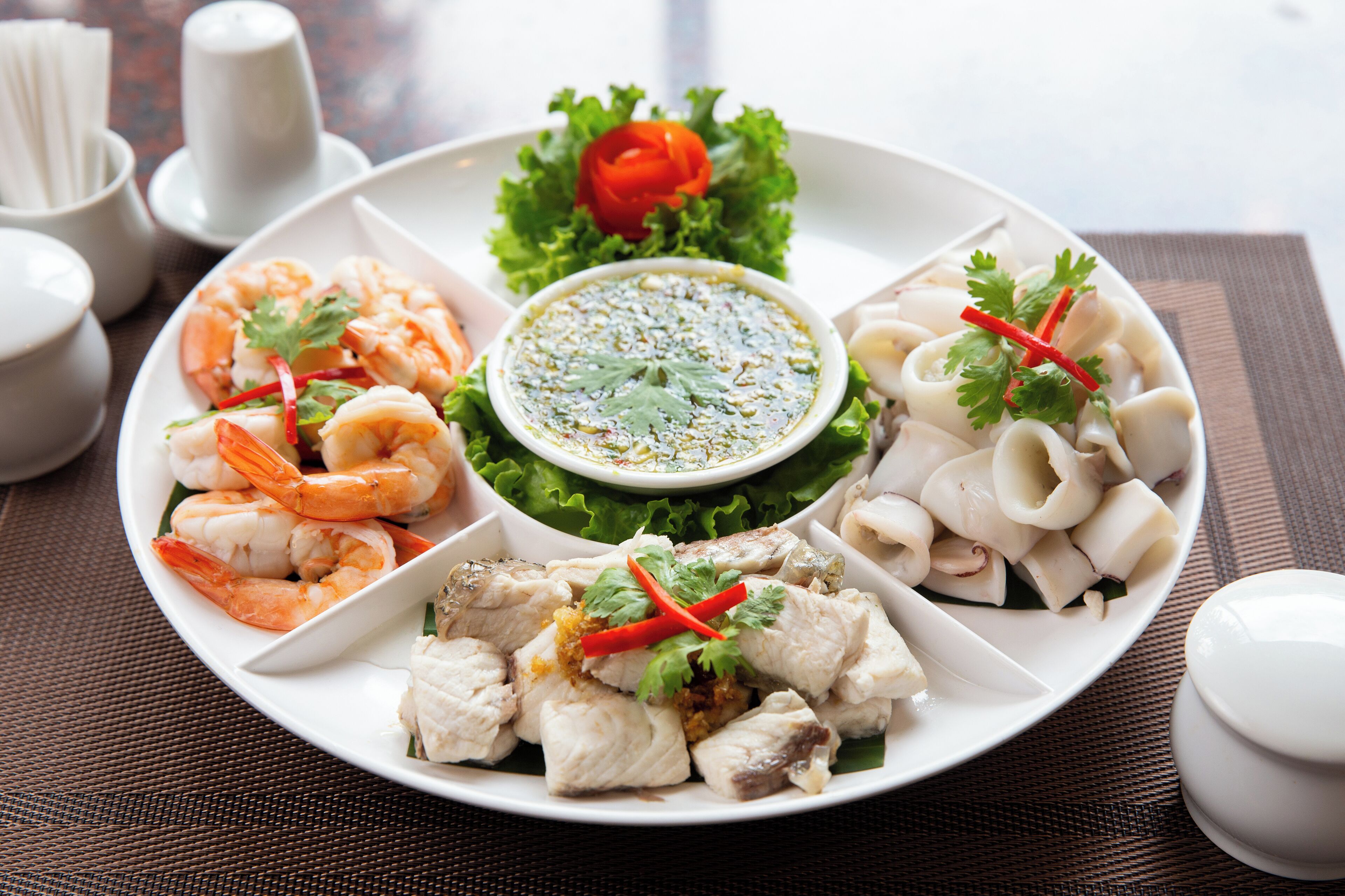 A plate of assorted seafood including shrimp, squid, and fish, served with a green sauce and garnished with herbs.