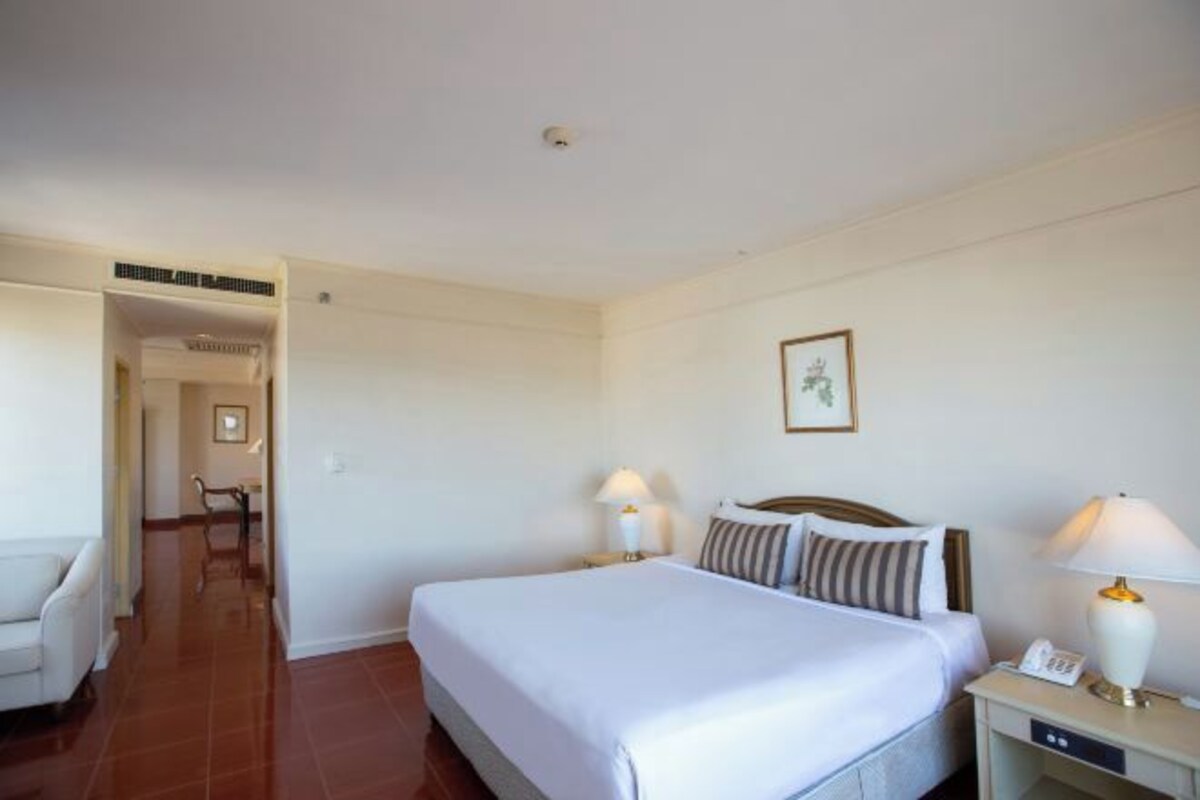 Une chambre d’hôtel avec un grand lit, deux tables de chevet avec des lampes, une chaise et une petite table avec un téléphone.