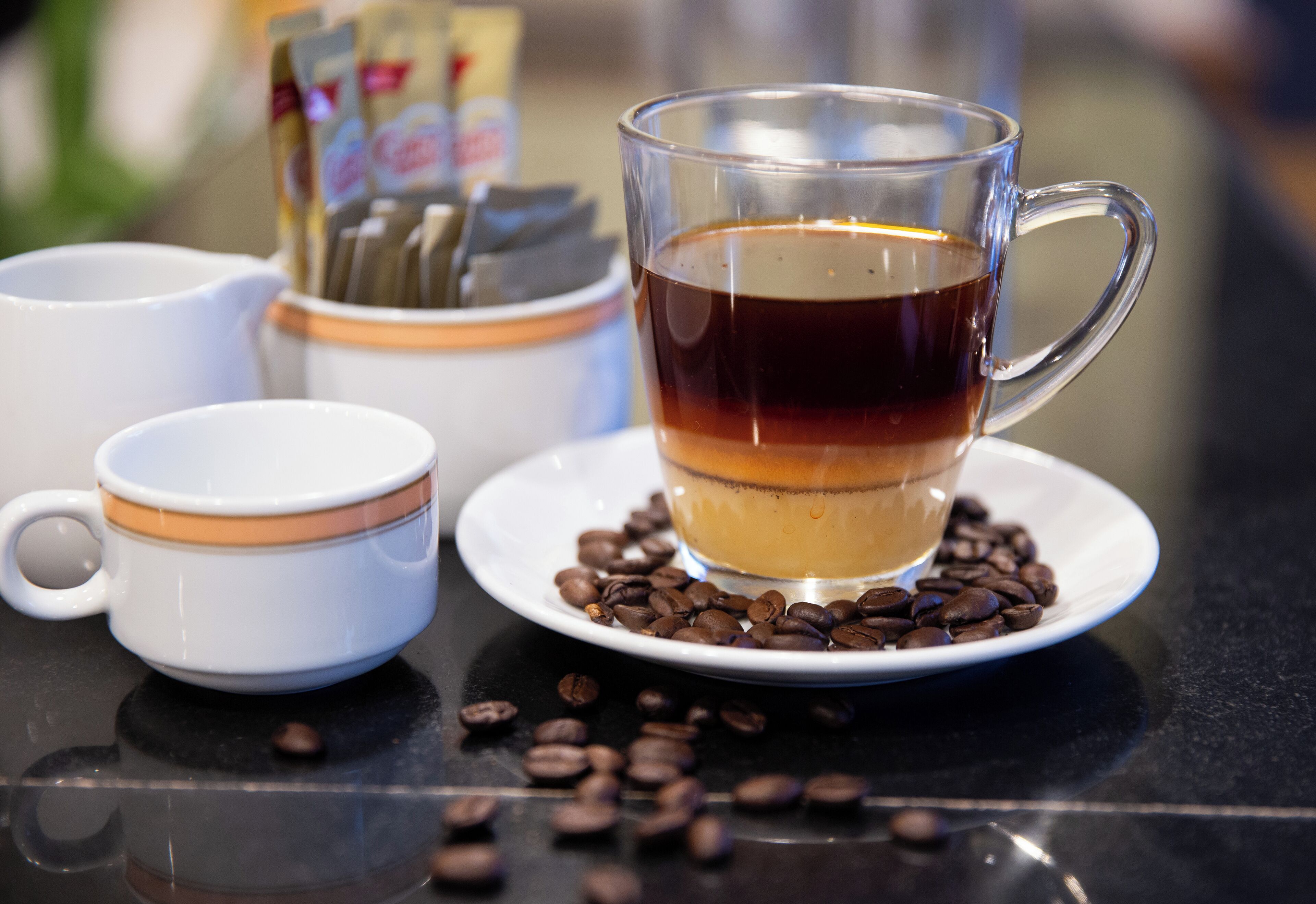 A glass cup of tea on a saucer surrounded by coffee beans.