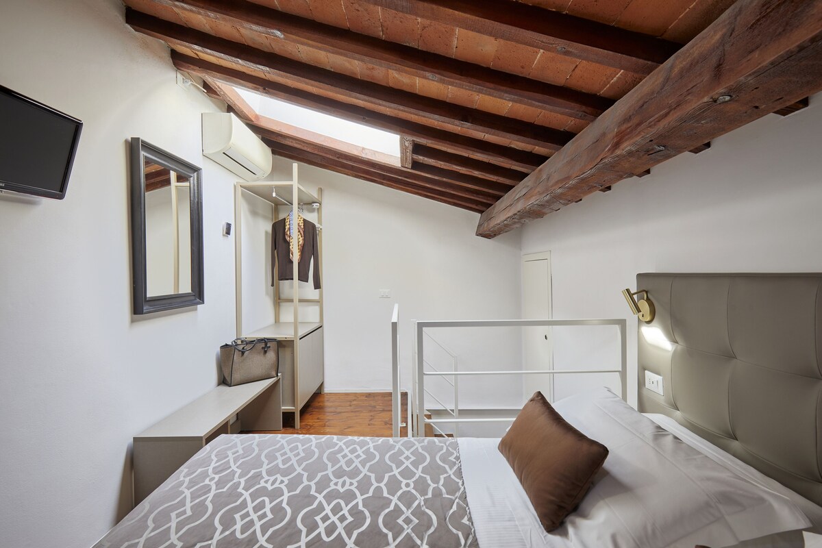 A bedroom with a bed, a bedside table, a mirror, a wardrobe, and a TV.